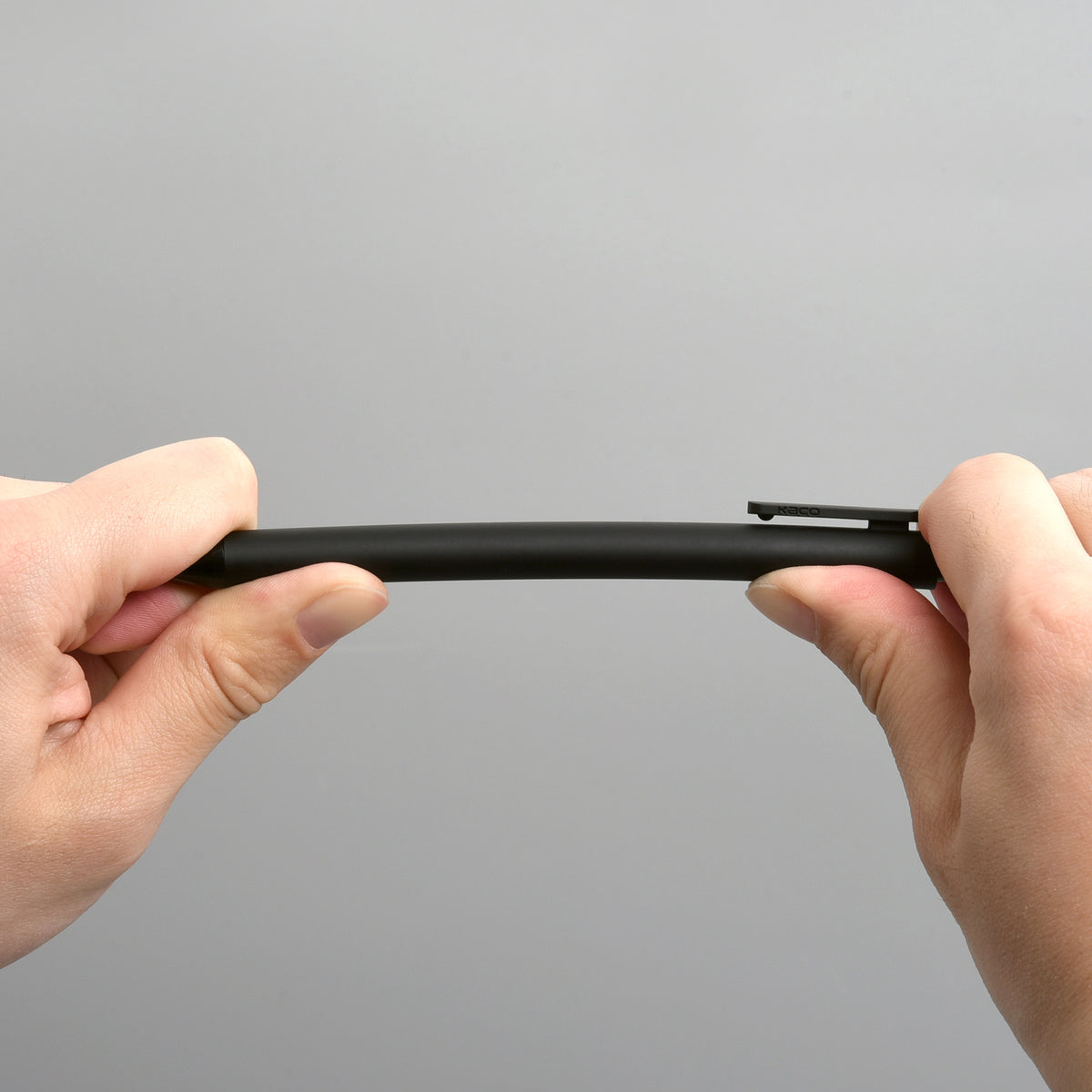 Two hands bending a black PURE gel pen against a grey background