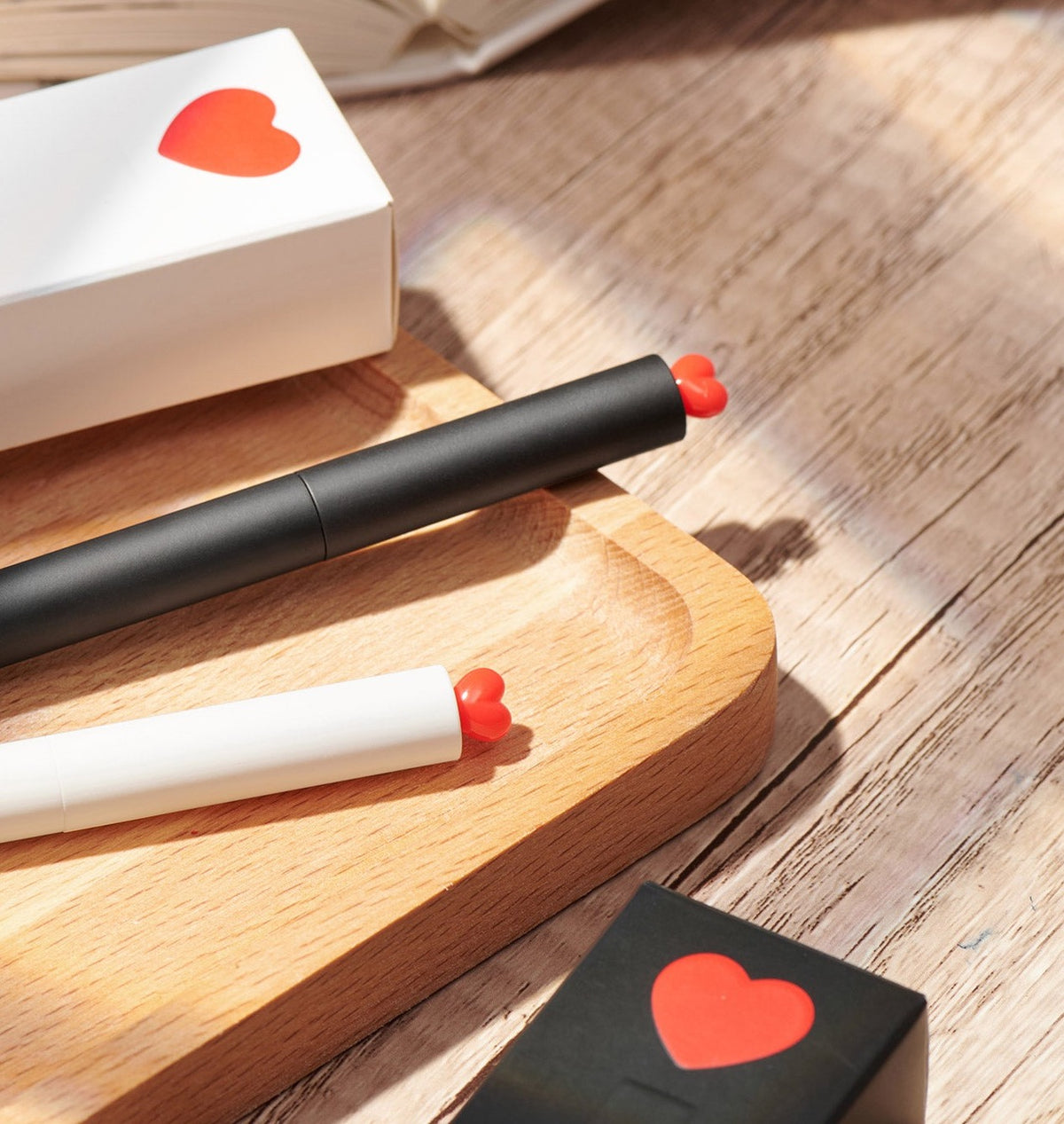 A black KACO gel pen with a red heart clip on a wooden tray